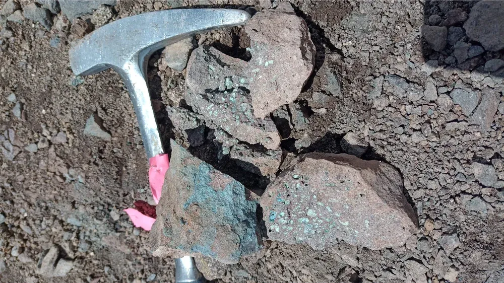Copper-mineralised rock outcrop with rock hammer for scale, Las Estrellas northern zone